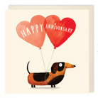 Illustrated greetings card featuring a black and tan dachshund, with two heart shaped balloons above it. The balloons are anchored by being tied around the dog’s torso. There is white capitalised text on the balloons. One reads “happy” and the other reads “anniversary”.