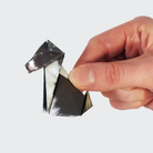 A hand holding a singular origami dog in a. Border Collie design against a white background.