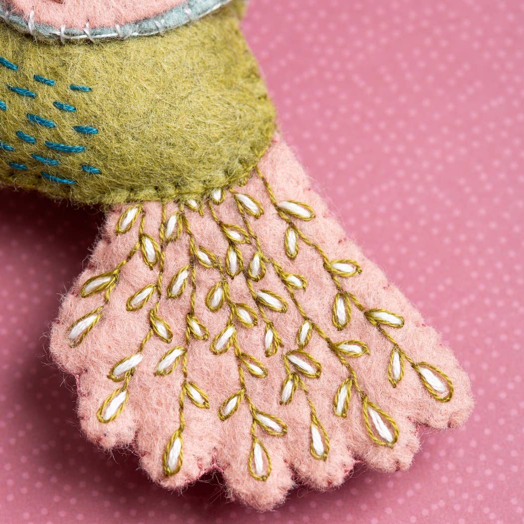 Close-up of a green embroidered hummingbird decoration on a pink polka dot background
