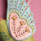 Close-up of a green embroidered hummingbird decoration on a pink polka dot background