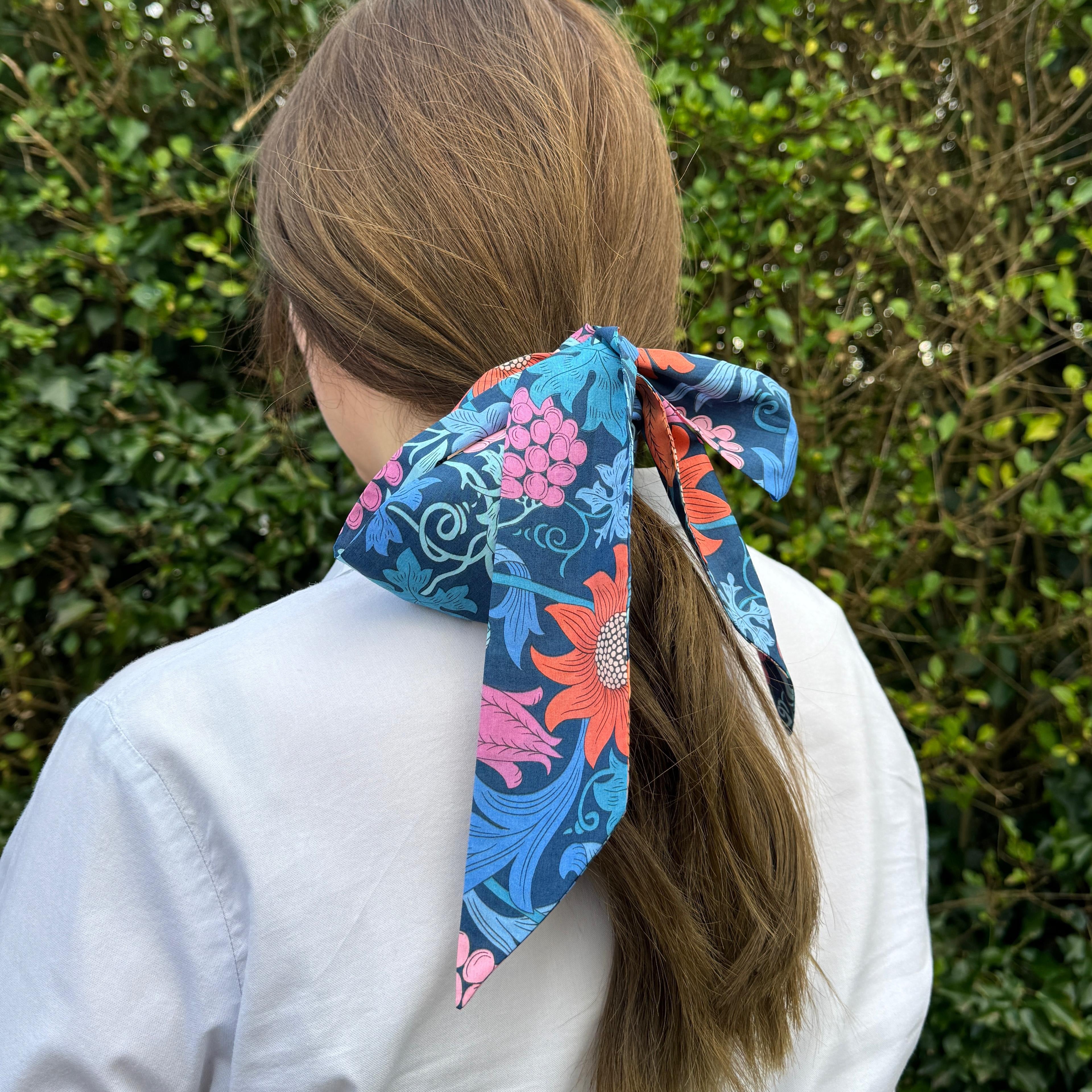Person wearing a colorful floral headscarf with a green leafy background