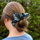 Person with a blue floral scrunchie in their hair against a green blurred background