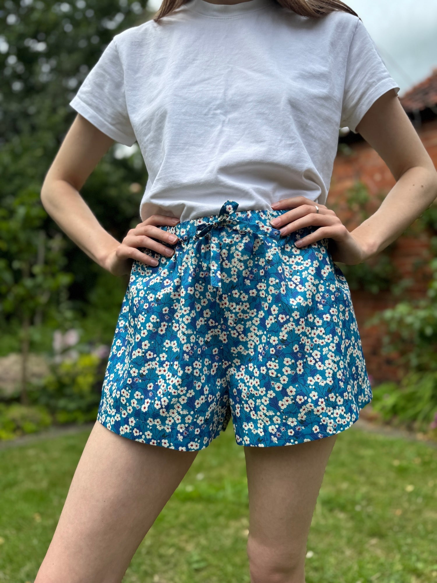 Person wearing blue floral shorts and a white t-shirt outdoors.