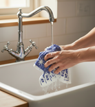 A blue and white swedish dishcloth being held under a running tap at a belfast sink