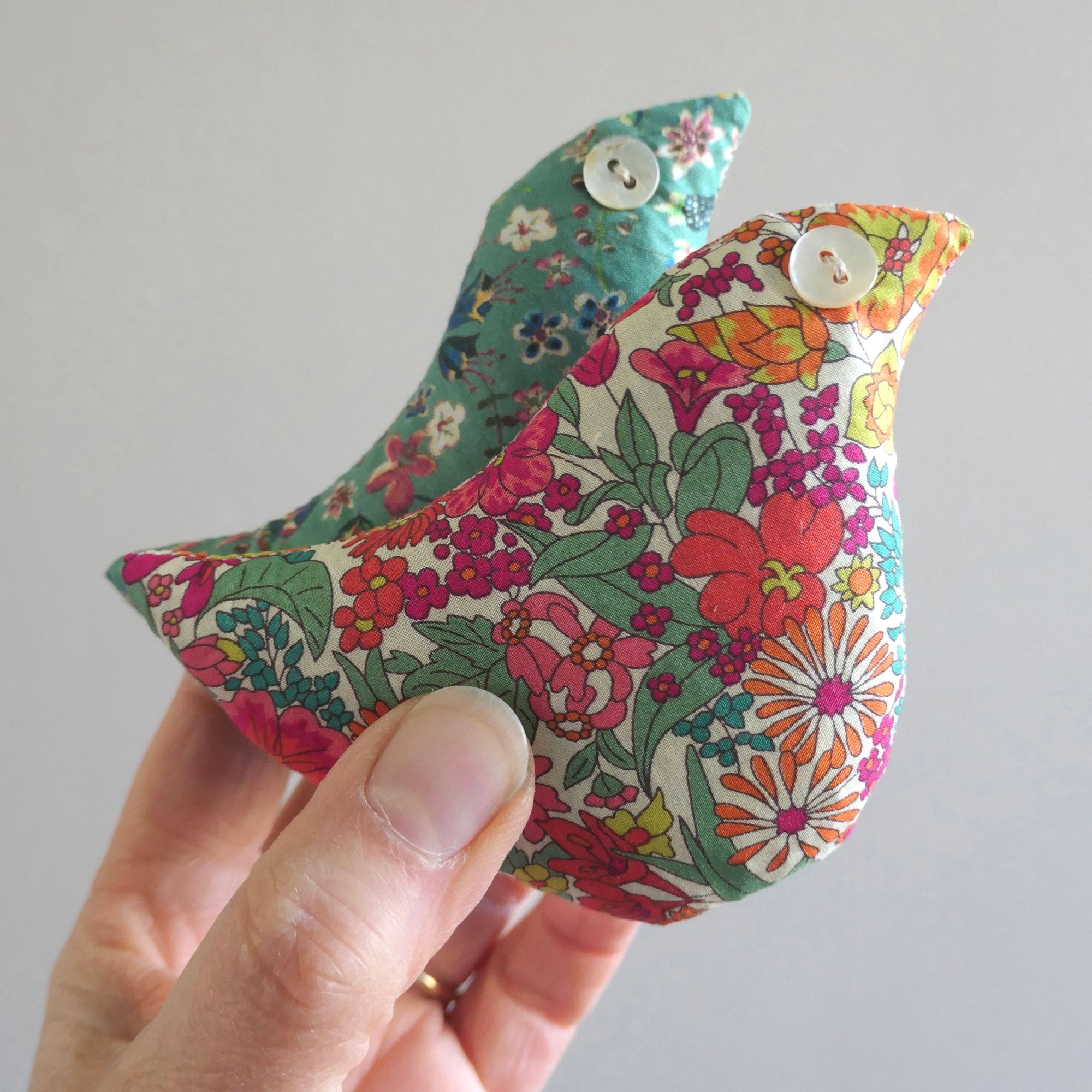 Handmade fabric birds with floral patterns held by a hand against a plain background