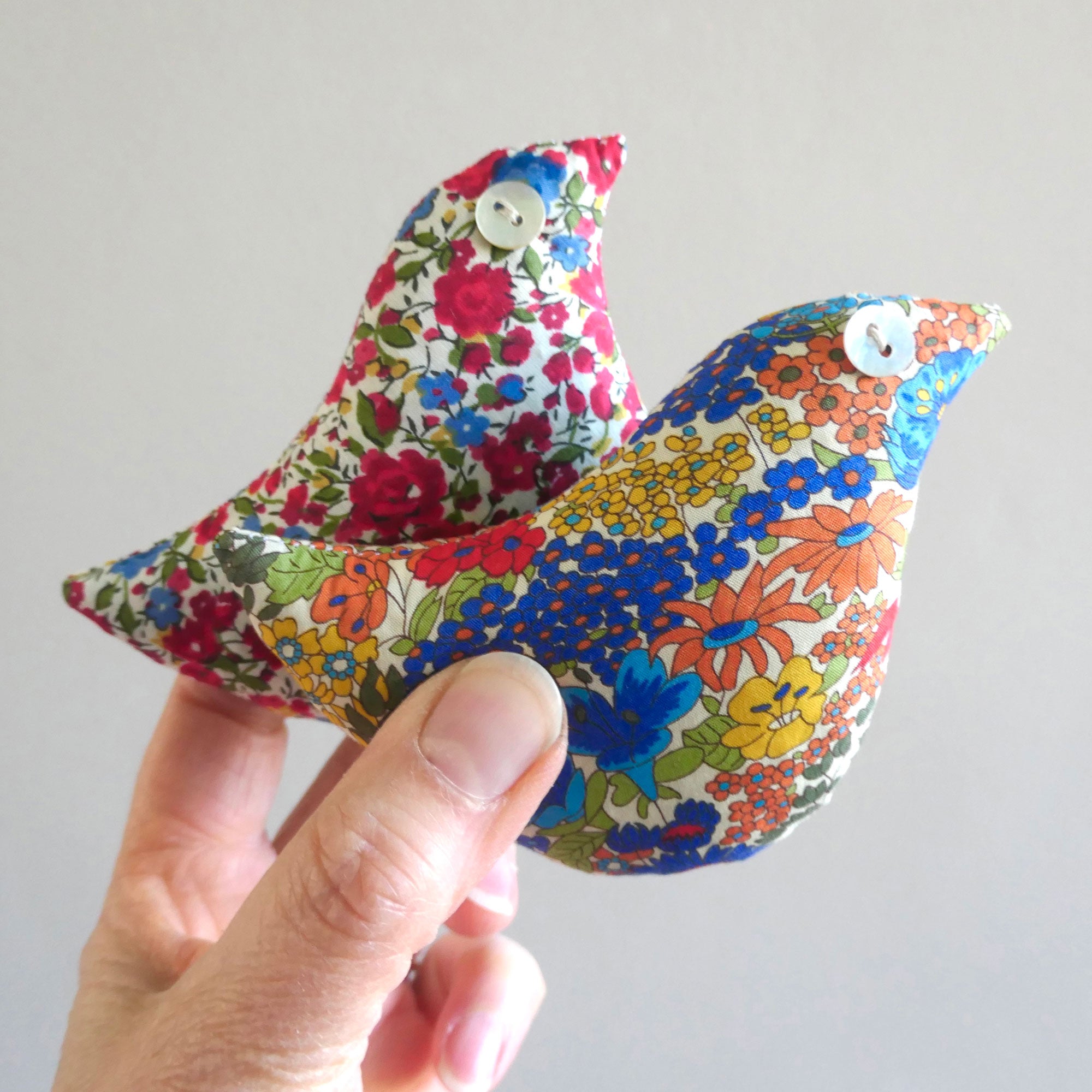 Colourful floral-patterned bird-shaped lavender sachets held by a hand against a plain background