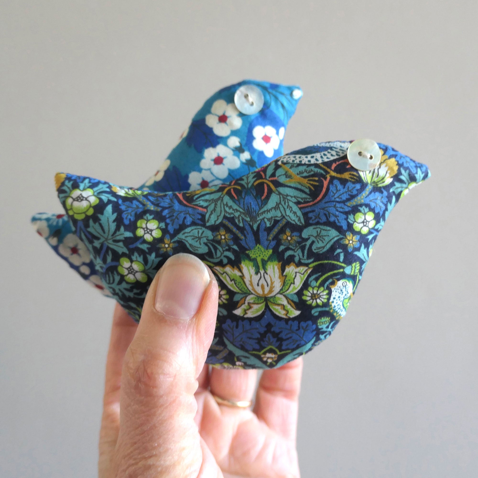 Handmade fabric bird with floral pattern held by a hand against a plain background