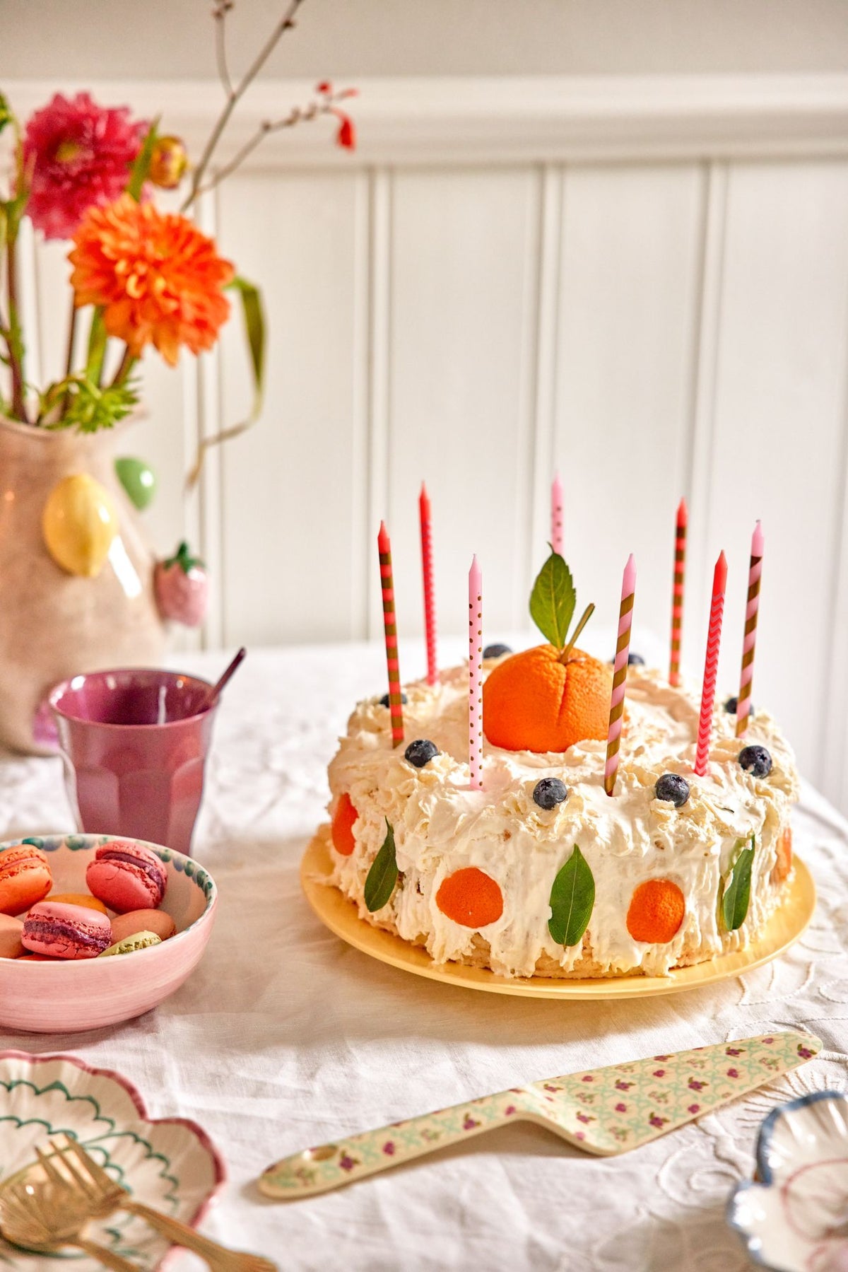 Decorative cake with candles on a table with flowers and a cup.