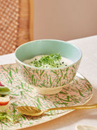 Bowl with green leafy garnish on a pink floral plate with a gold spoon