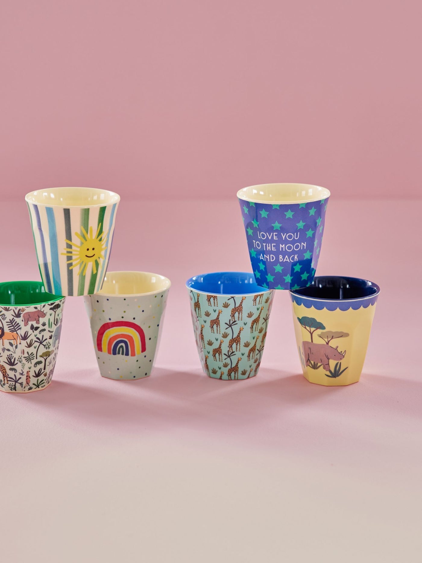Set of colorful children's cups with various designs on a pink background