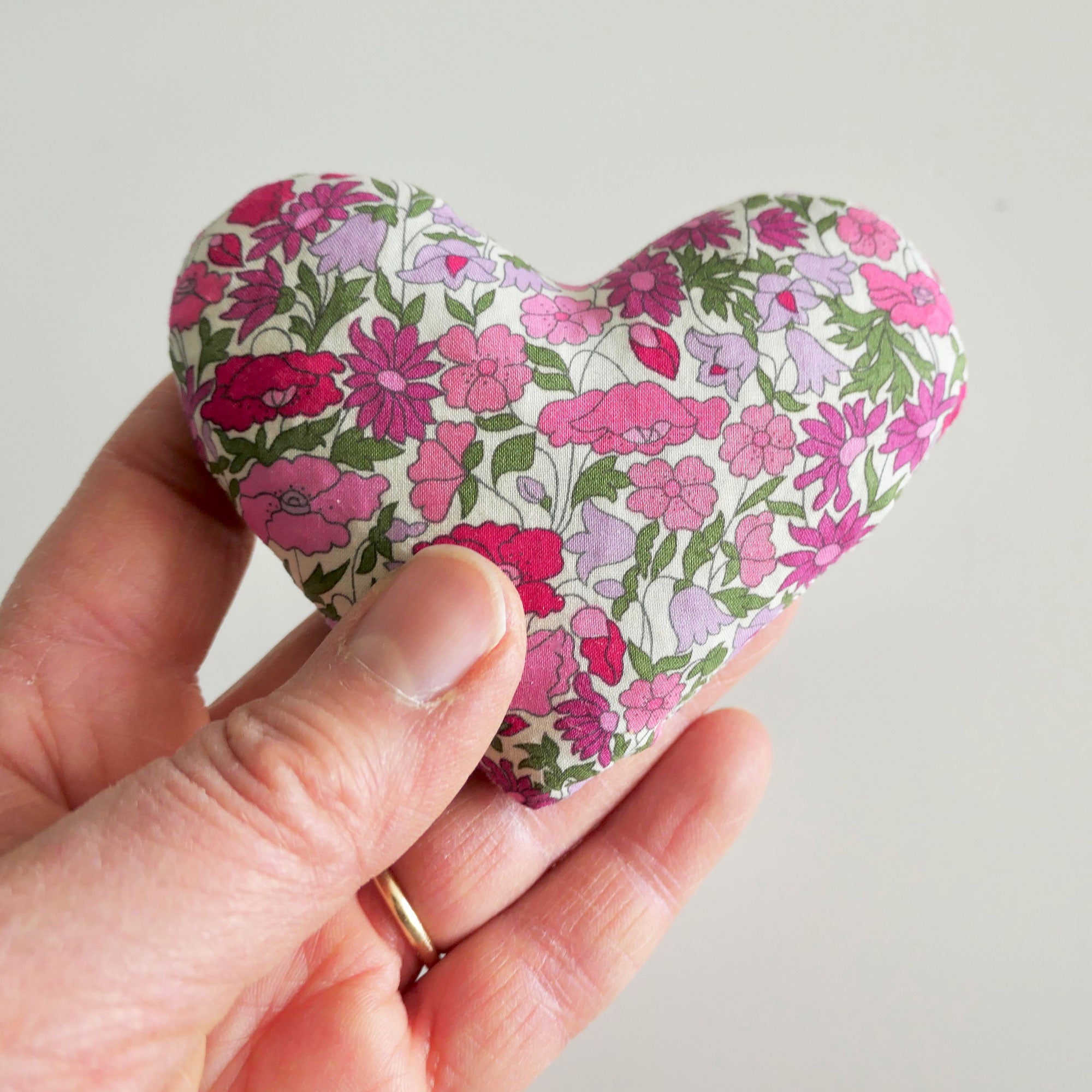 Hand holding a floral-patterned heart-shaped sachet against a plain background