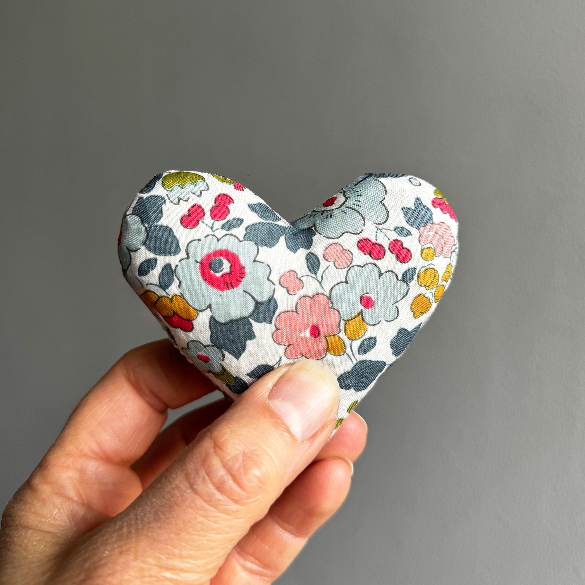 Hand holding a floral-patterned heart-shaped sachet against a grey background