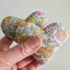Hand holding a floral-patterned heart-shaped fabric sachet against a plain background