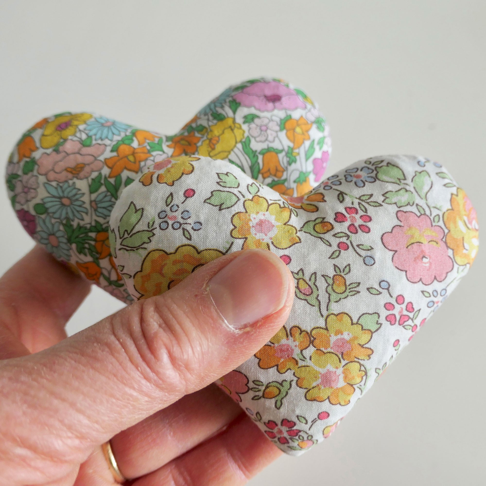 Hand holding a floral-patterned heart-shaped fabric sachet against a plain background