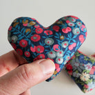 Hand holding a floral-patterned heart-shaped fabric sachet against a white background