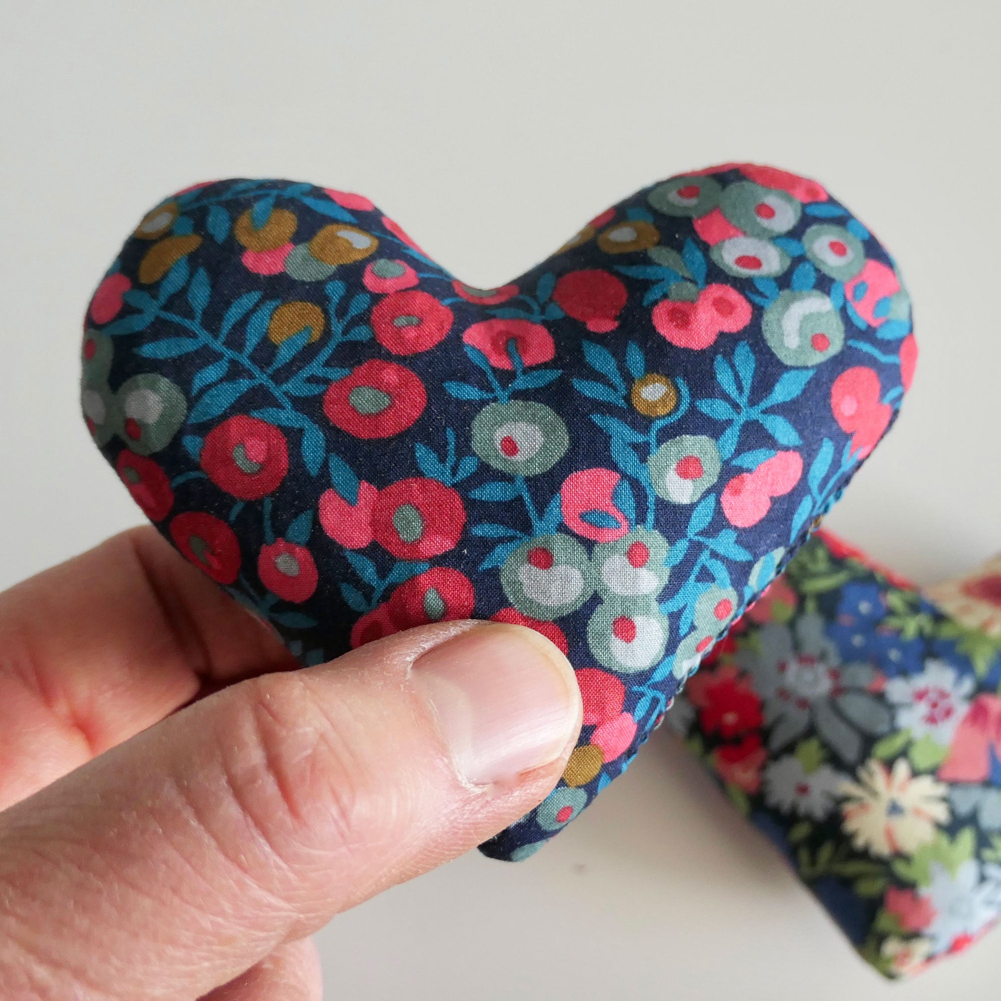 Hand holding a floral-patterned heart-shaped fabric sachet against a white background