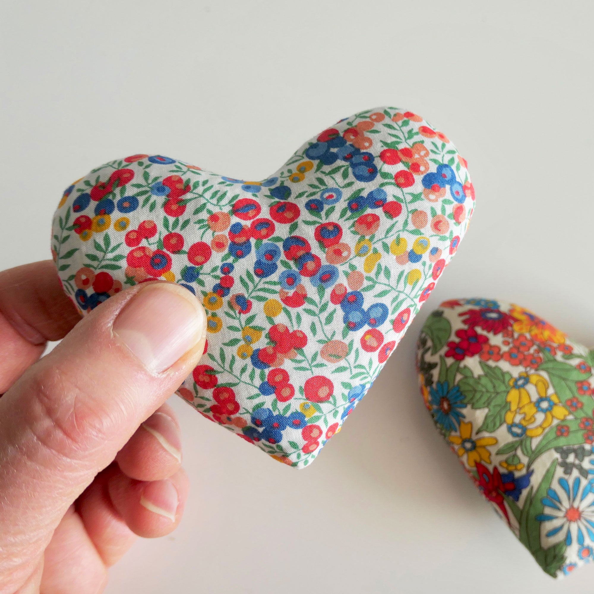 Hand holding a floral-patterned heart-shaped fabric sachet on a light background