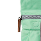 Close-up of a green bag with a grey zipper and brown leather pull tab on a white background