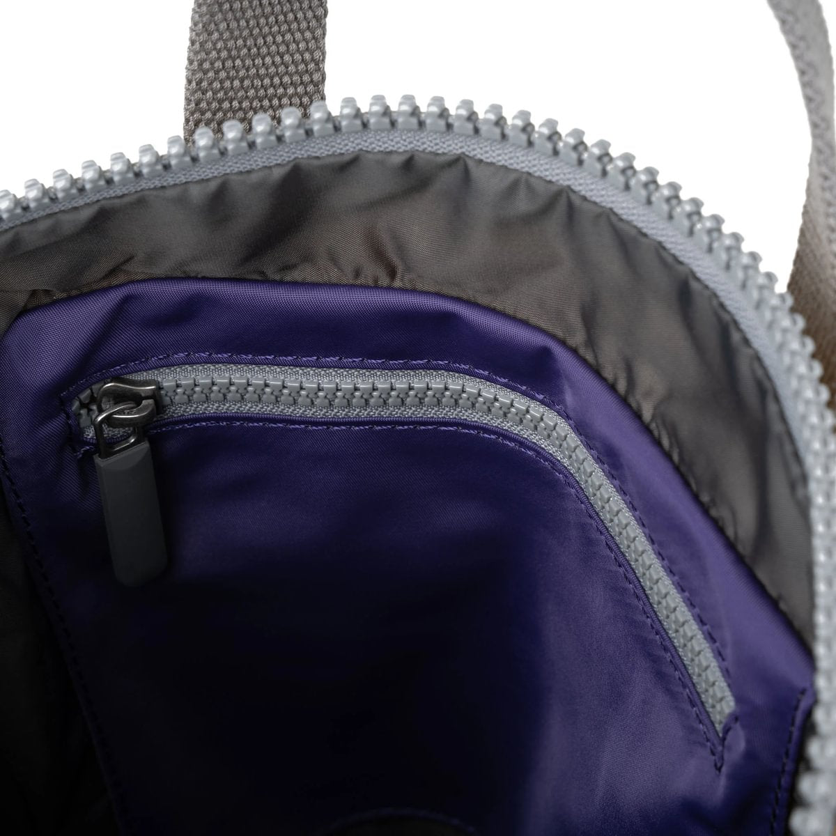 Close-up of a purple bag, showing the inside of the bag with a zipper pocket, shown on a white background