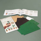 Packaging, instructions manual and cut paper sheets on a light green background.