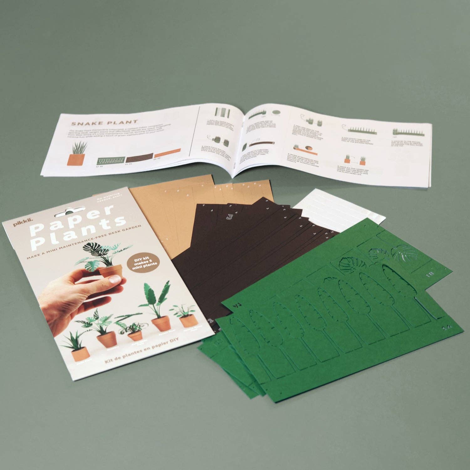 Packaging, instructions manual and cut paper sheets on a light green background.