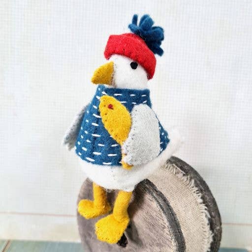 Stuffed toy seagull wearing a red hat and blue sweater on a textured surface.