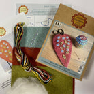 Kraft packaging with final product image, colourful threads, needle, red, green and blue felt sheets and an instructions sheet. 