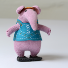 A knitted plush mouse character standing on a white surface against a light grey background. The plush has pink knit ears and legs, a blue vest with white embroidered stitching', and black shoes.