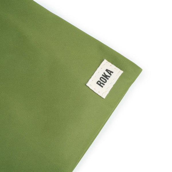 A close up photo of the bottom corner of a avocado green bag, showing the ROKA London label.