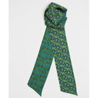 A green necktie with a detailed floral and geometric pattern, styled in a loop at the top and laid flat below, shown against a plain light gray background.