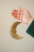 Hand holding a decorative moon-shaped ornament with star patterns against a neutral background