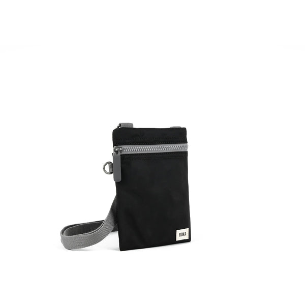 A photo of the front and side of a small rectangular black pocket bag. It has a grey zip horizontally at the top, grey straps, and a small ROKA logo in the bottom right corner.