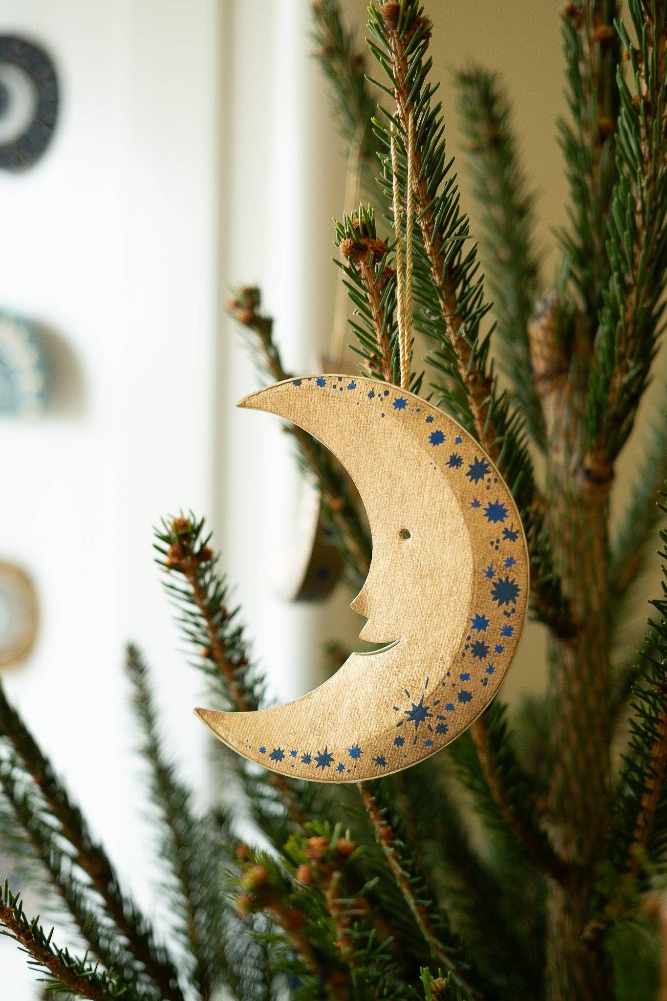 Wooden moon-shaped ornament with star patterns hanging on a Christmas tree.