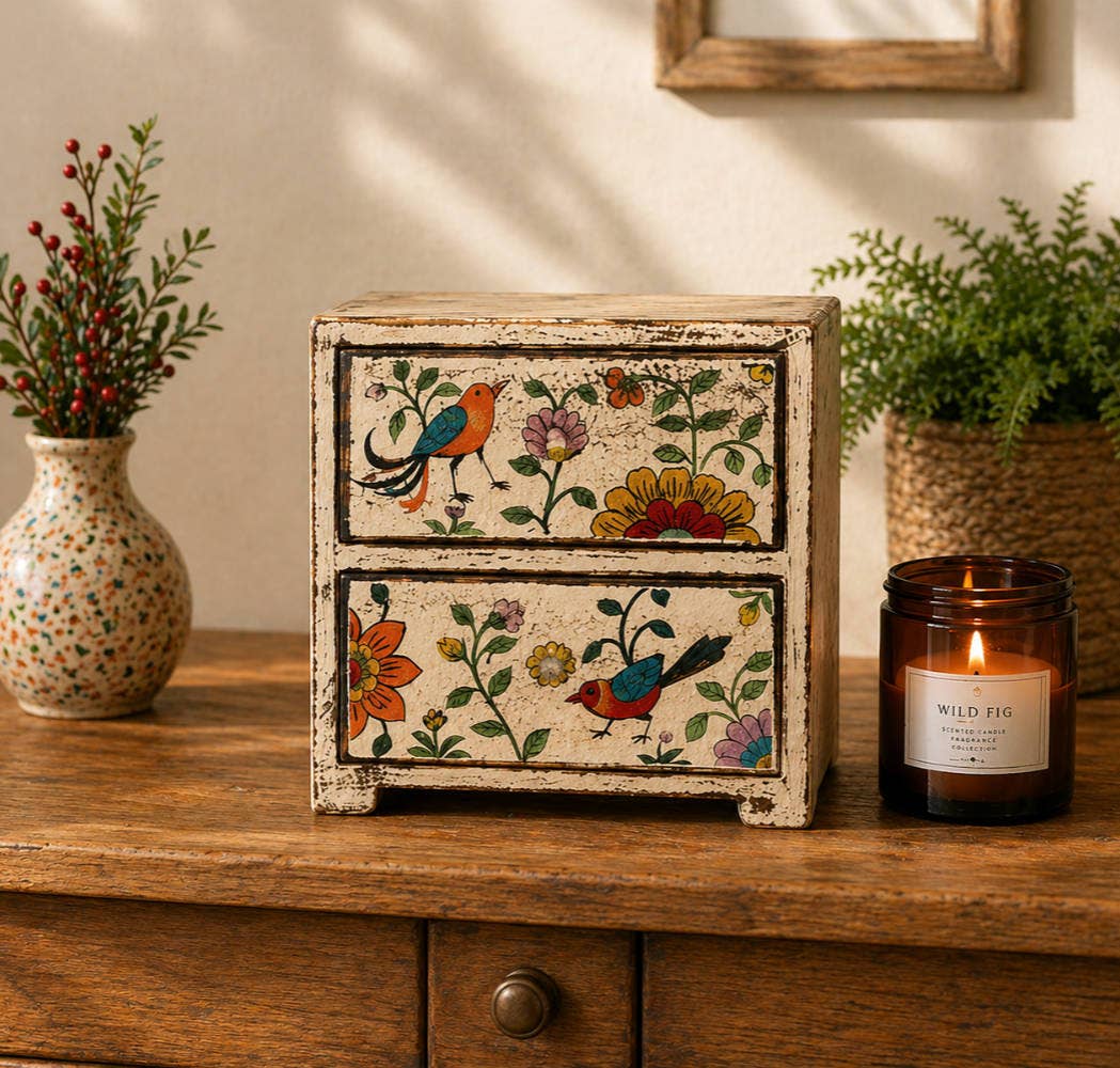 Decorative wooden box with floral and bird patterns on a wooden surface with a candle and vase in the background.