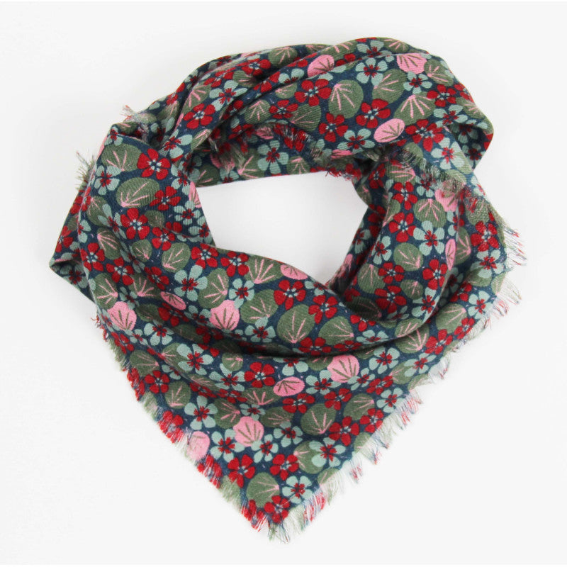 A fringed scarf with a dense floral pattern in red, pink, and green on a dark teal background, displayed on a clean white background.