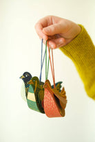 Colorful duck-shaped tea infusers hanging from a string held by a hand.
