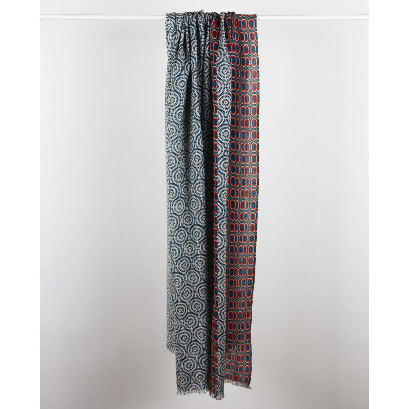 A long scarf with two vertical panels of intricate geometric and circular patterns, hanging from a white rod against a plain light gray wall.