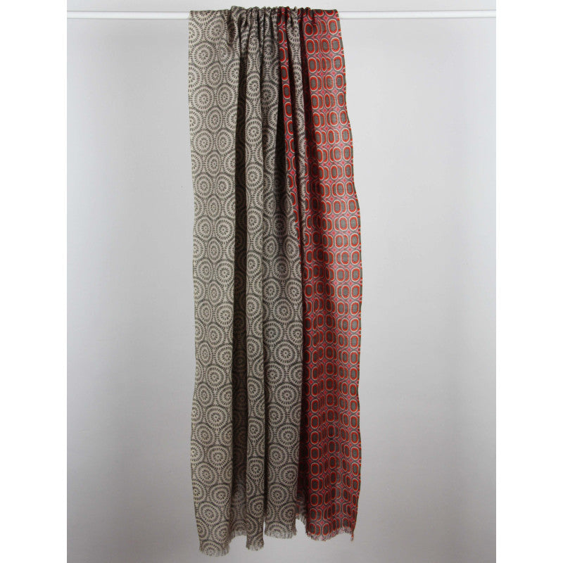 Two long patterned fabric panels hanging side by side against a plain light gray background. The left panel is taupe with a circular spiral pattern, and the right panel is rust red with a repeating geometric circle motif.