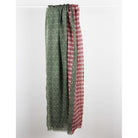 A long fabric panel or curtain with a split design, featuring a sage green side with a circular pattern and a dusty red side with a geometric pattern, hanging from a white rod against a white background.
