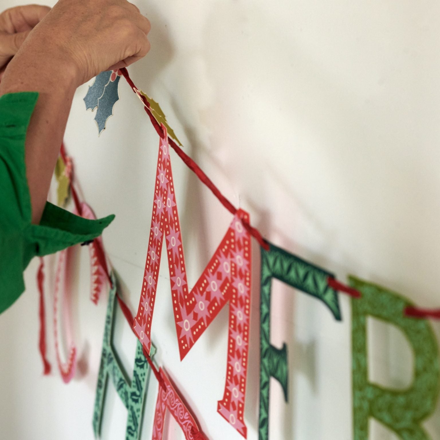 Person hanging a decorative banner with letters on a white wall