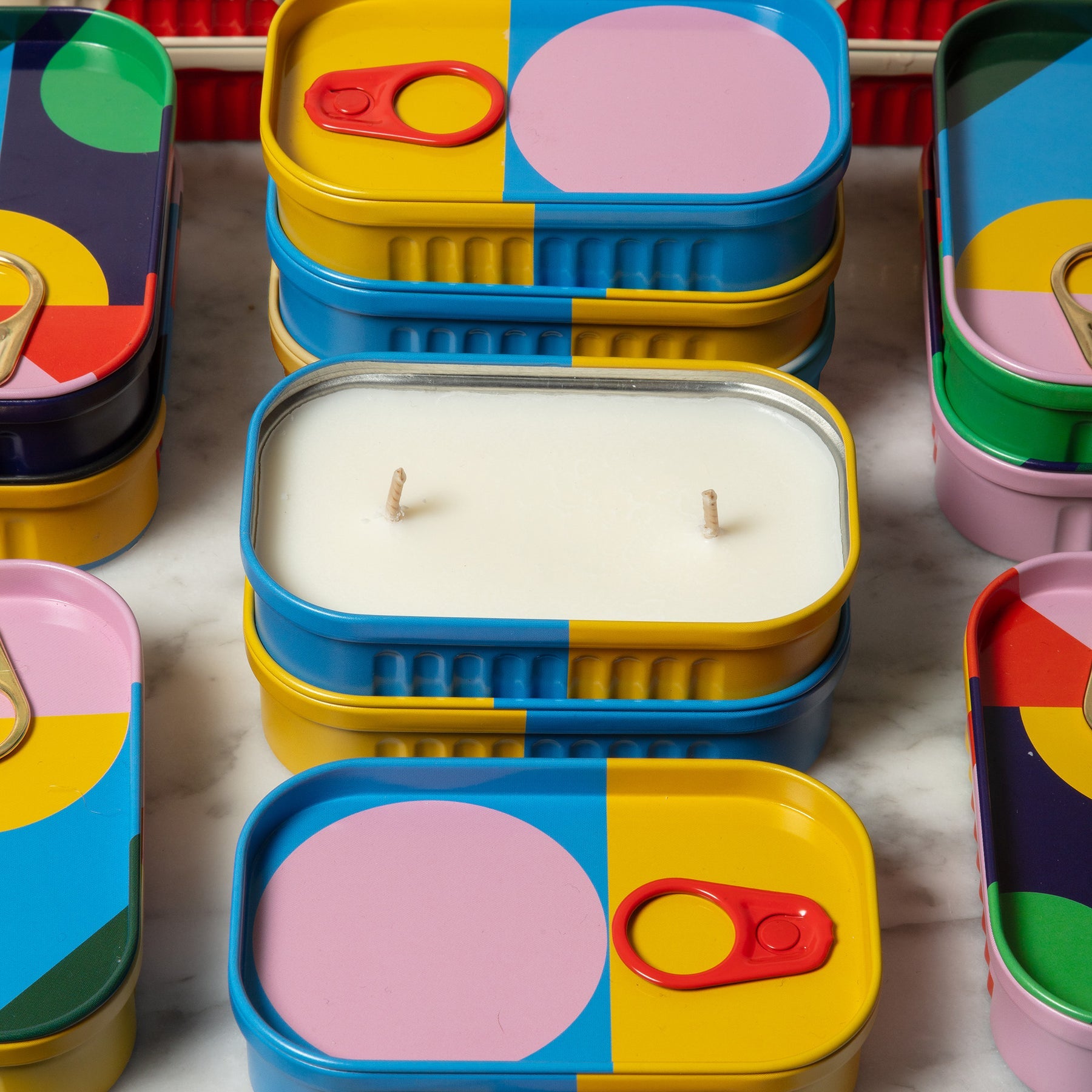 Colorful tin containers with a candle inside on a light surface