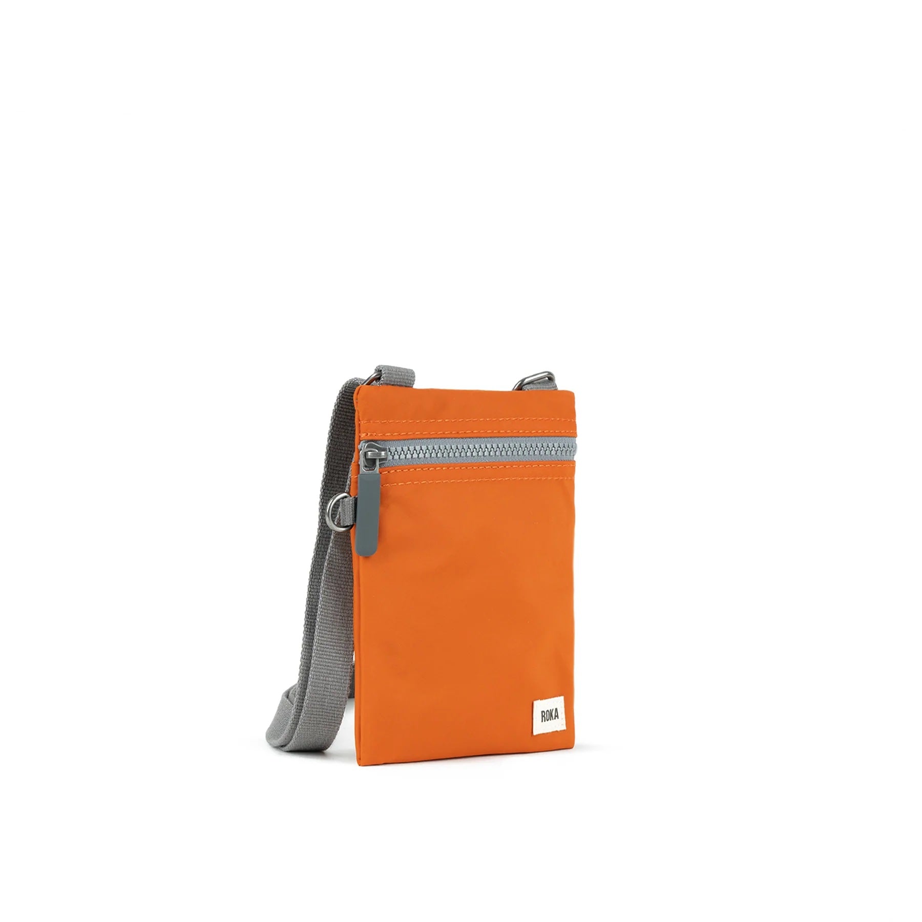 A photo of the front and side of a small rectangular orange pocket bag. It has a grey zip horizontally at the top, grey straps, and a small ROKA logo in the bottom right corner.