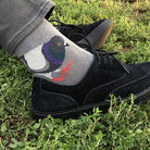 A person wearing a gray crew sock with a colorful bird graphic and black suede shoes, standing on green grass outdoors.